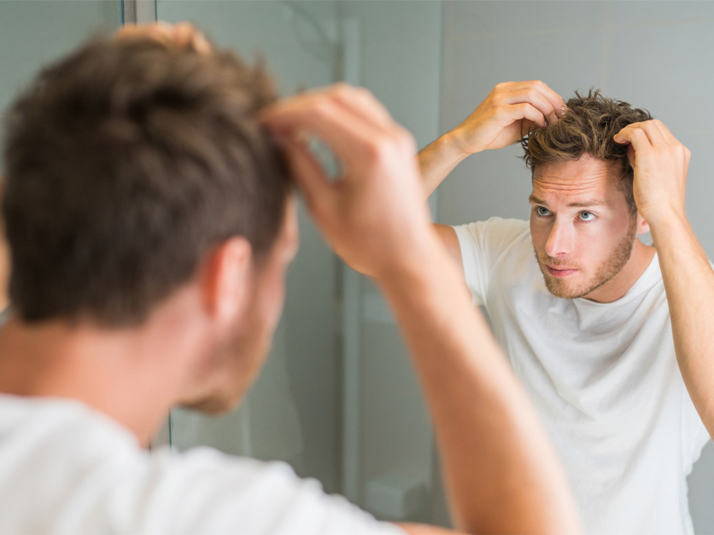 Man looking at his hair in mirror, hair loss, hair growth, ness healthcare